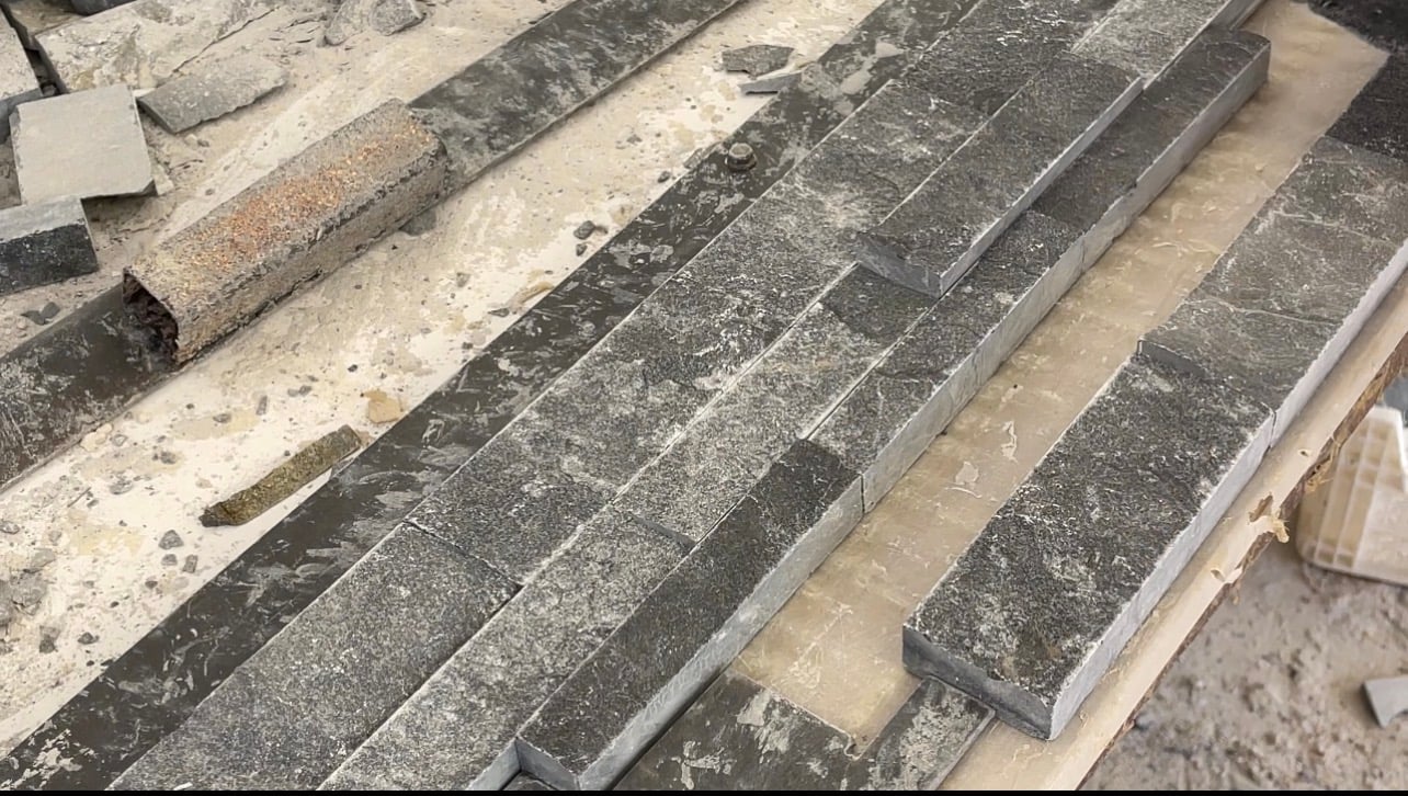 Rows of dark split-face stone strips laid out side by side on a workshop bench.