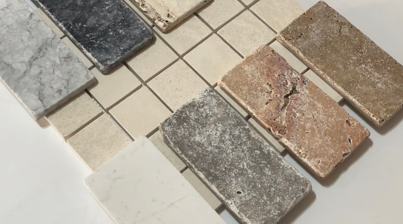 Tumbled and honed natural stone pieces in white, grey, black, cream and rust laid across a sheet of small square mosaic tiles.