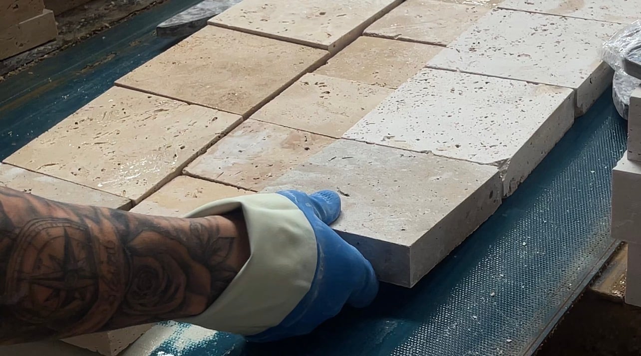 A gloved hand pressing pale, pitted rectangular stone tiles into line on a work surface.