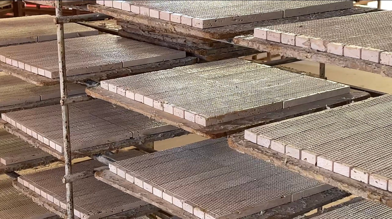 Mesh-backed sheets of small white square tiles resting in rows on wooden racks.