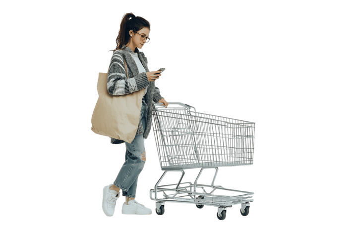 Young woman uses her phone while shopping with reusable tote bag and shopping cart.