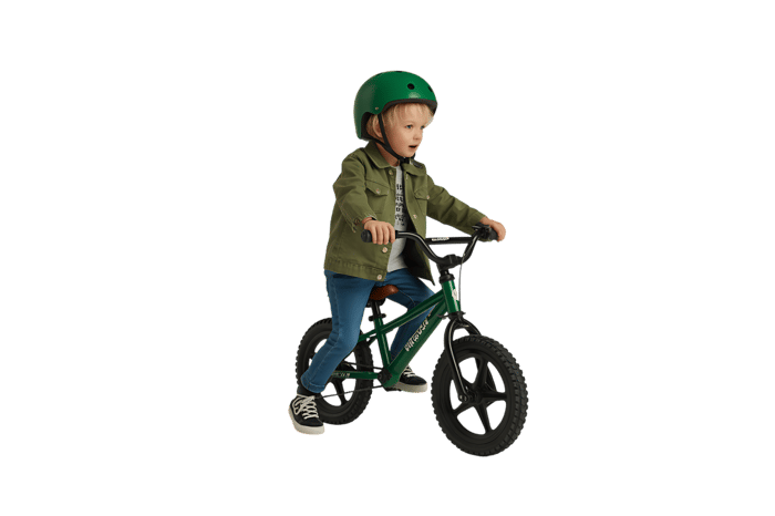 Young child riding green balance bike with helmet