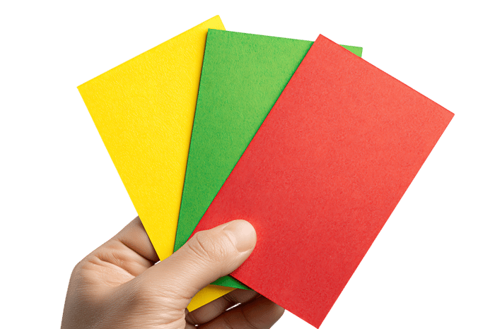 Close up of a hand holding yellow, green and red referee cards.