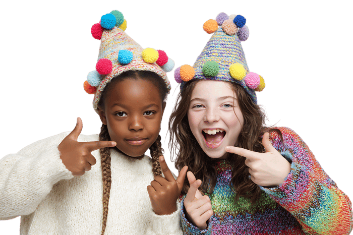 Two girls in colorful hats point at themselves.
