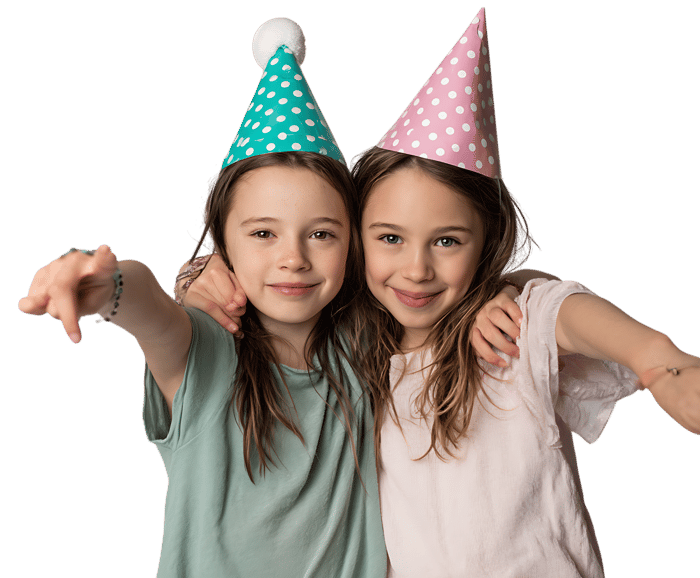 Two girls in party hats point at the camera.