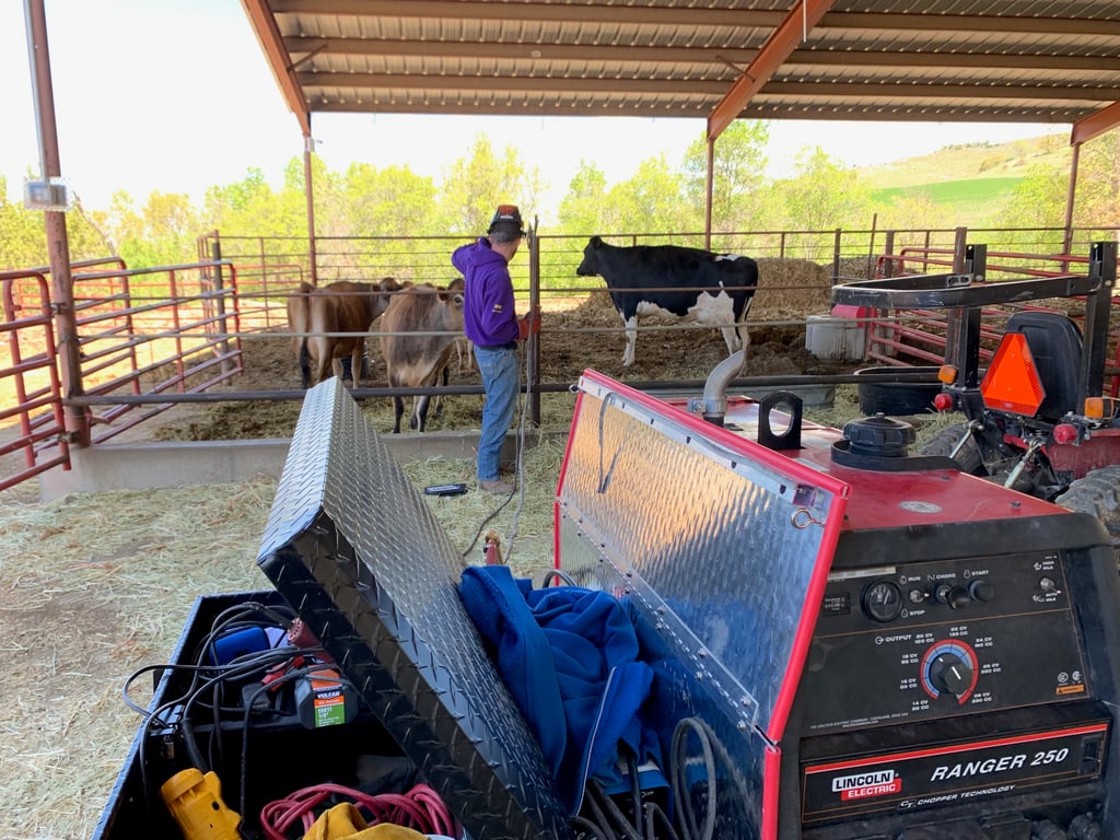Jimmie working on a metal fence inside an open cow barn with his mobile welding rig in the foreground