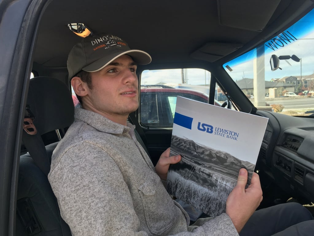 Derek sits in the passenger seat of a car holding paperwork from a local bank.
