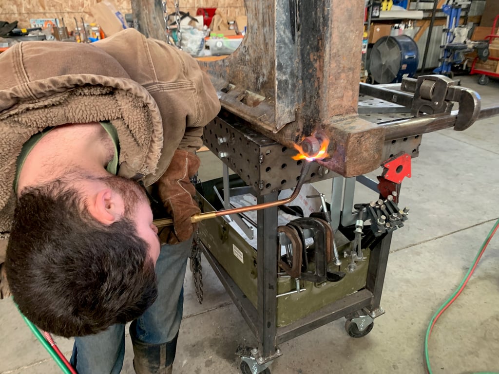 Jimmie with his head inverted, holding an oxygen-propane torch, heating a bolt on some equipment
