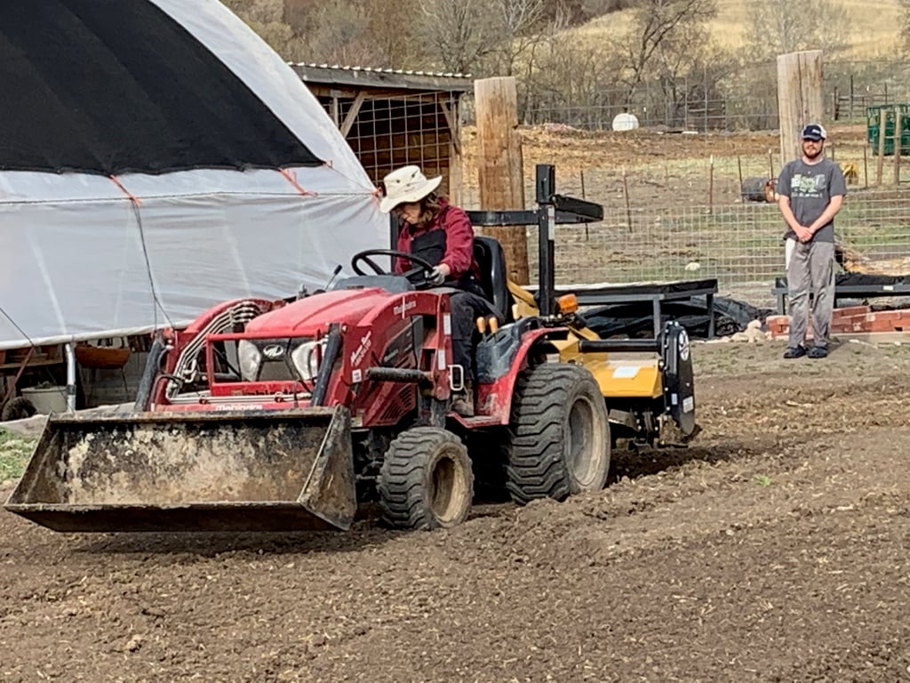 Derek watches a small tractor pulling a tiller as it makes repeated passes through the garden