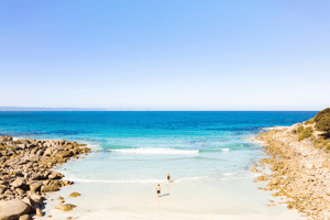 A couple enjoying a refreshing swim in the clear blue waters of Kangaroo Island, surrounded by stunning coastal scenery. The sun shines brightly overhead as they embrace the beauty of nature and create lasting memories together