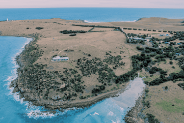Aerial image looking back at Sea Dragon Lodge accommodation with Pink Bay in the foreground and Cape Willoughby Lighthouse in the distance on Kangaroo Island