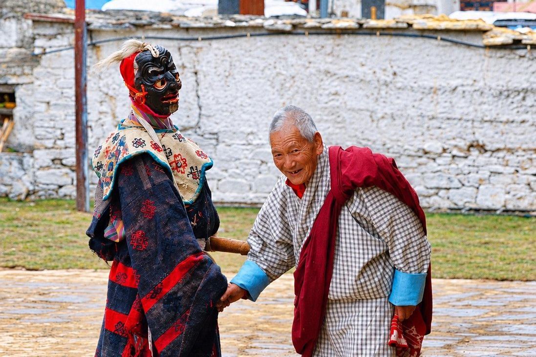 A masked atsara, the festival clown, greeting an elderly Bhutanese man at a tshechu