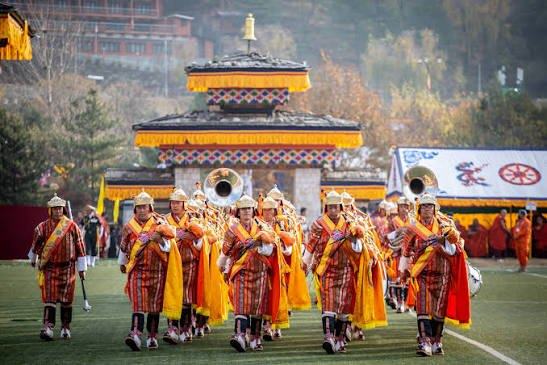 A ceremonial band in traditional dress and helmets, marching at a celebration in Bhutan.