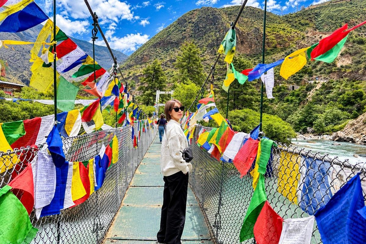 Traveller on a suspension bridge hung with prayer flags over a river in Bhutan