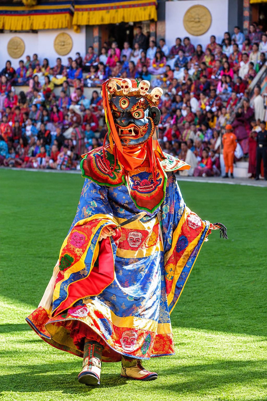 A cham dancer in a skull-crowned mask and blue brocade robes dancing before a packed crowd at a Bhutanese tshechu