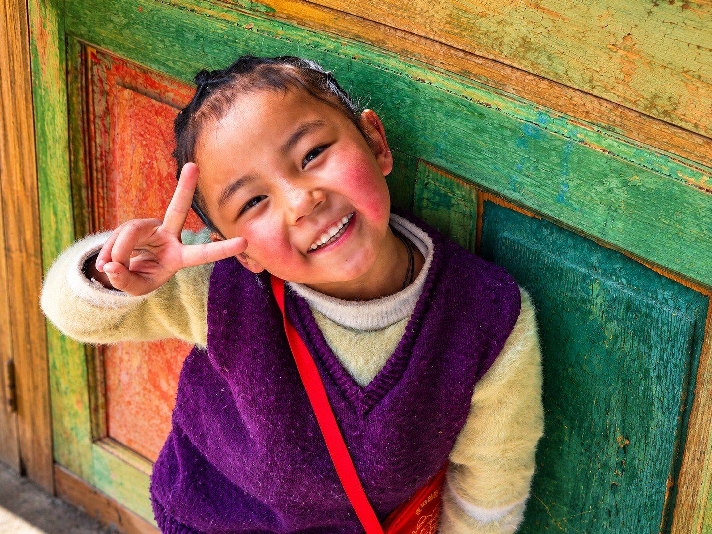 A smiling young girl beside a painted wooden door in Bhutan