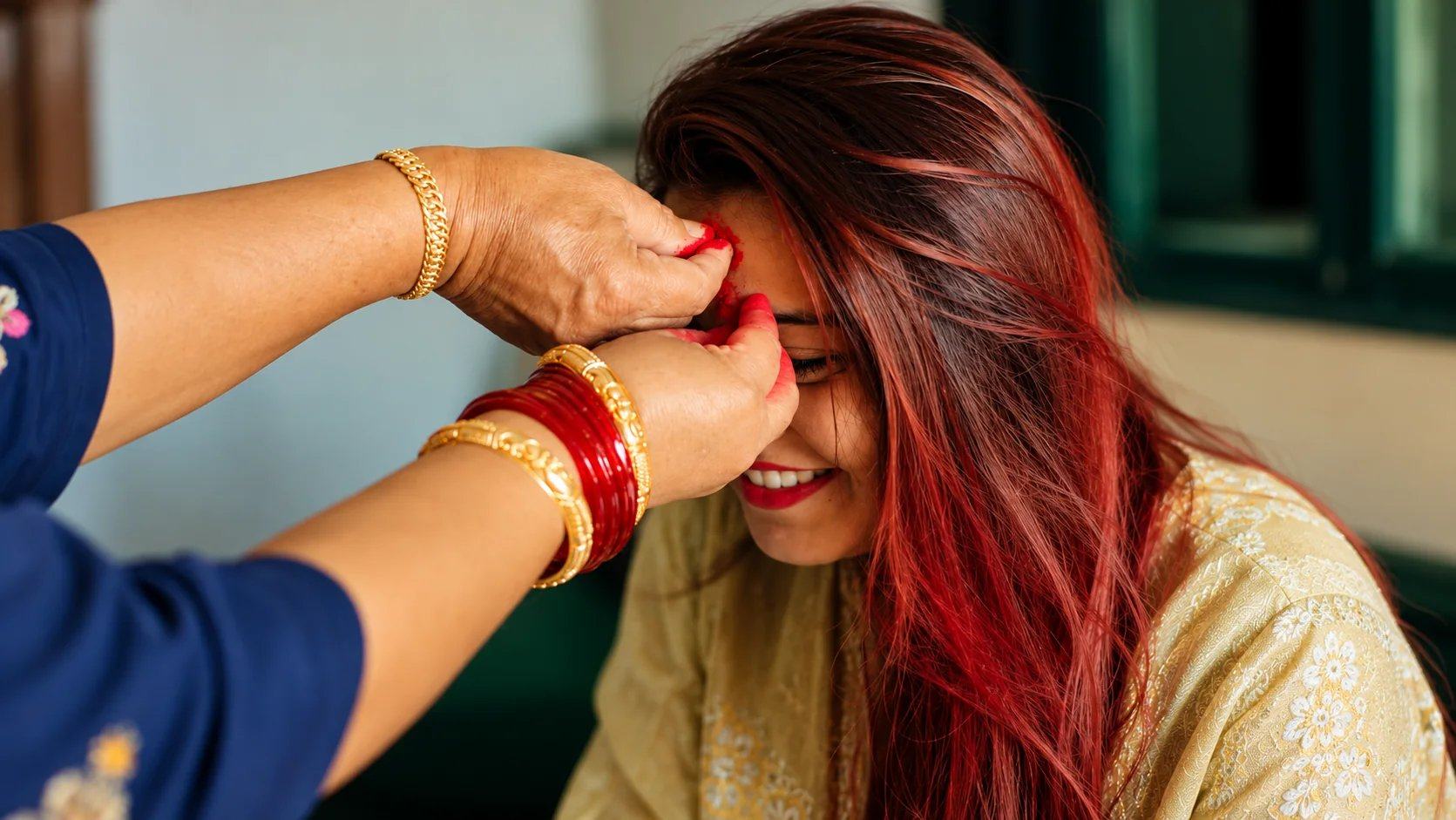 A woman's hands pressing red tika onto a smiling young woman's forehead on Vijaya Dashami, Nepal