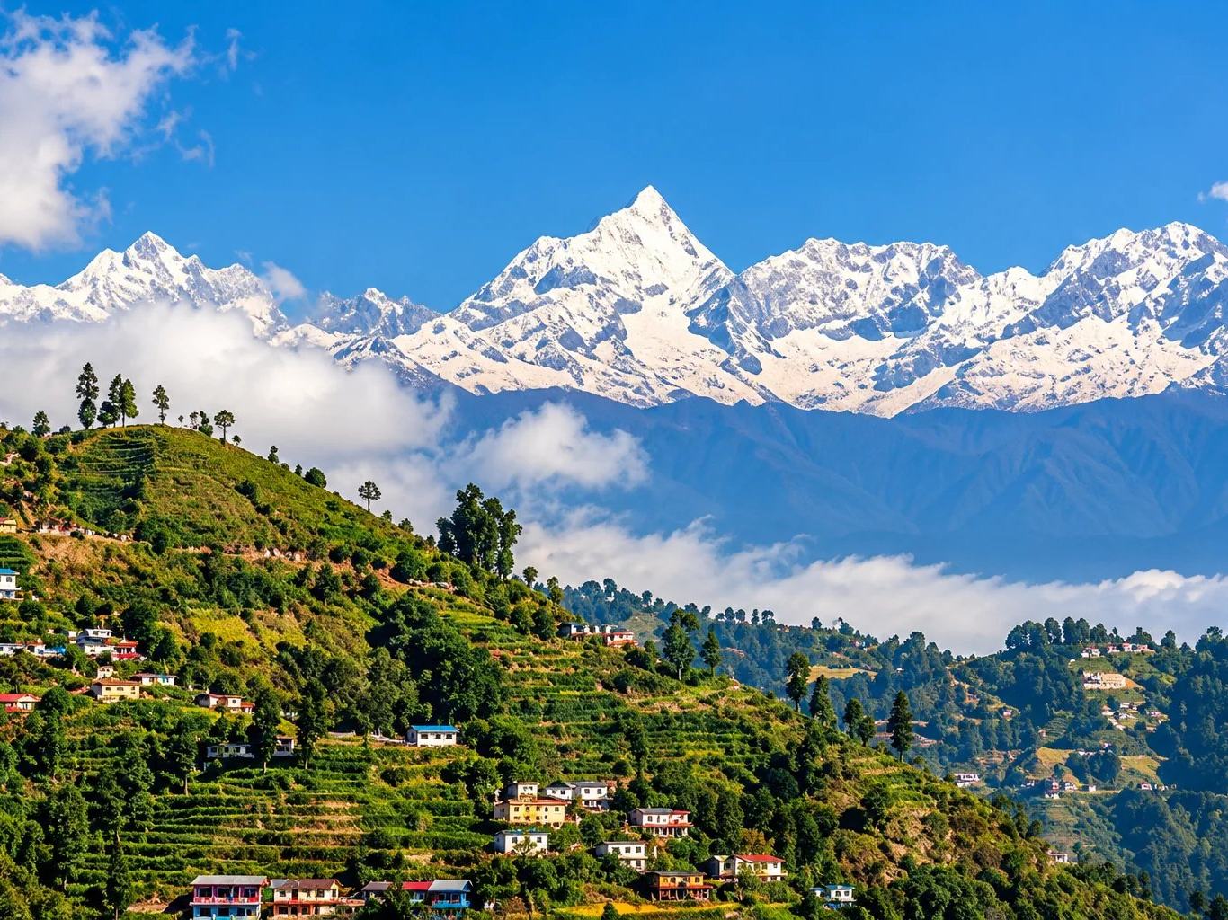 A terraced hill village on a green ridge below a line of snow-capped Himalayan peaks, Nepal
