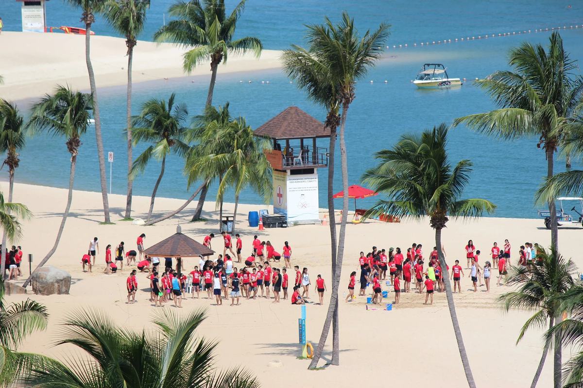 Palms, a lifeguard tower and a group on the sand at Siloso Beach, Singapore