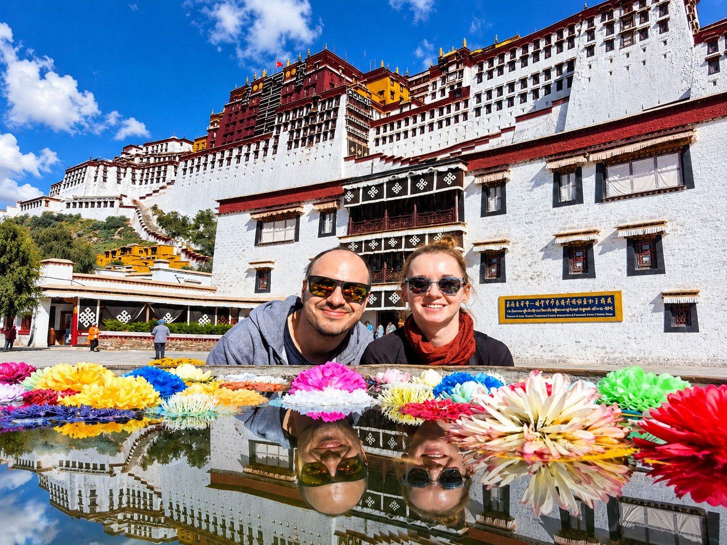 Two travellers smiling by the reflecting pool in front of the Potala Palace