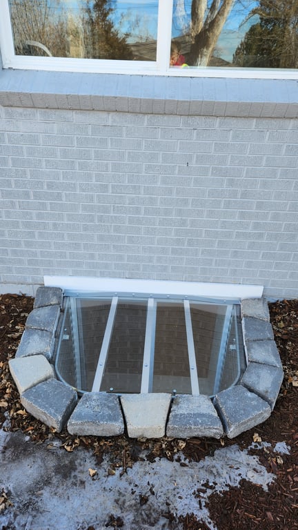 Clear polycarbonate window well cover with locks installed on a brick surrounded window well in Erie Colorado