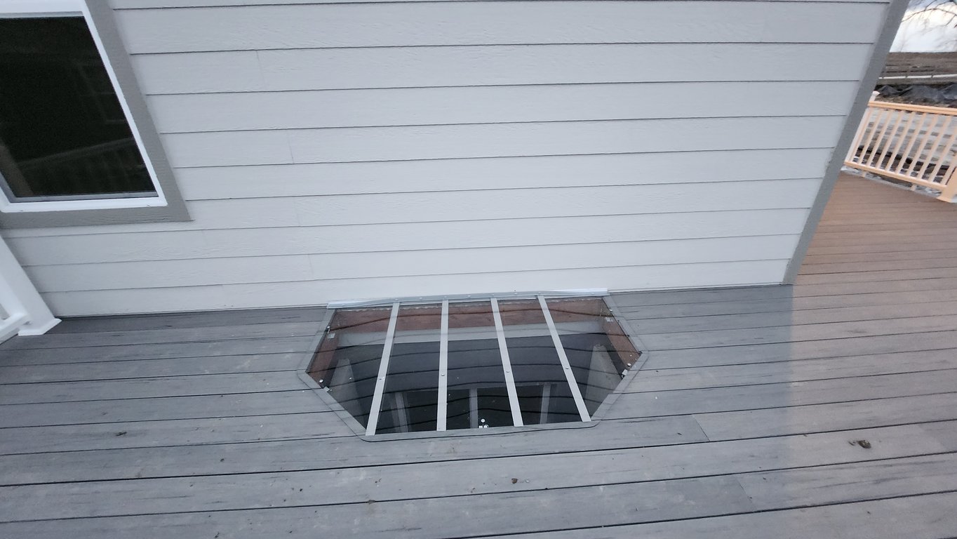 Clear polycarbonate window well cover installed near an open deck in Wheat Ridge Colorado