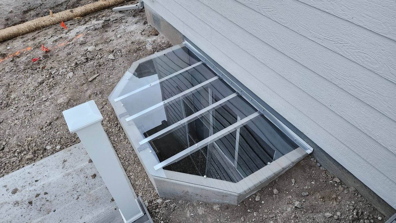 Sloped clear polycarbonate window well cover installed on a concrete window well in Johnstown Colorado
