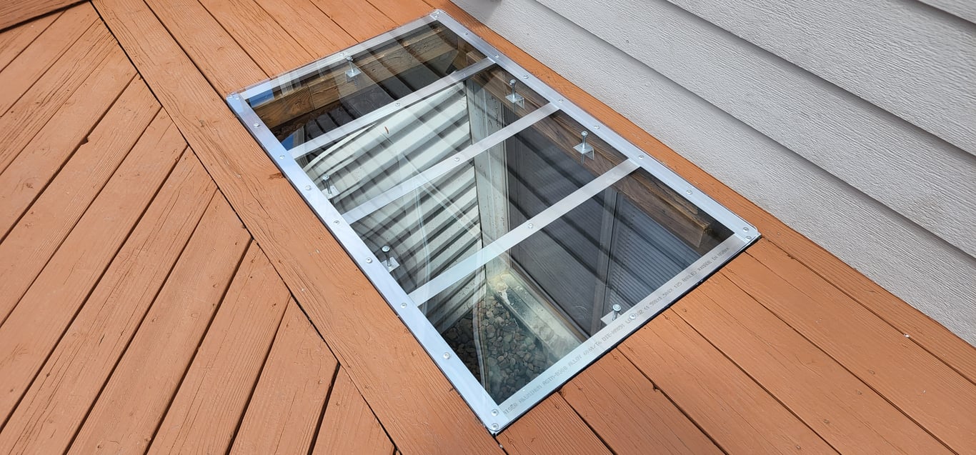 Custom clear polycarbonate window well cover installed under a deck in Arvada Colorado made to fit any size or shape