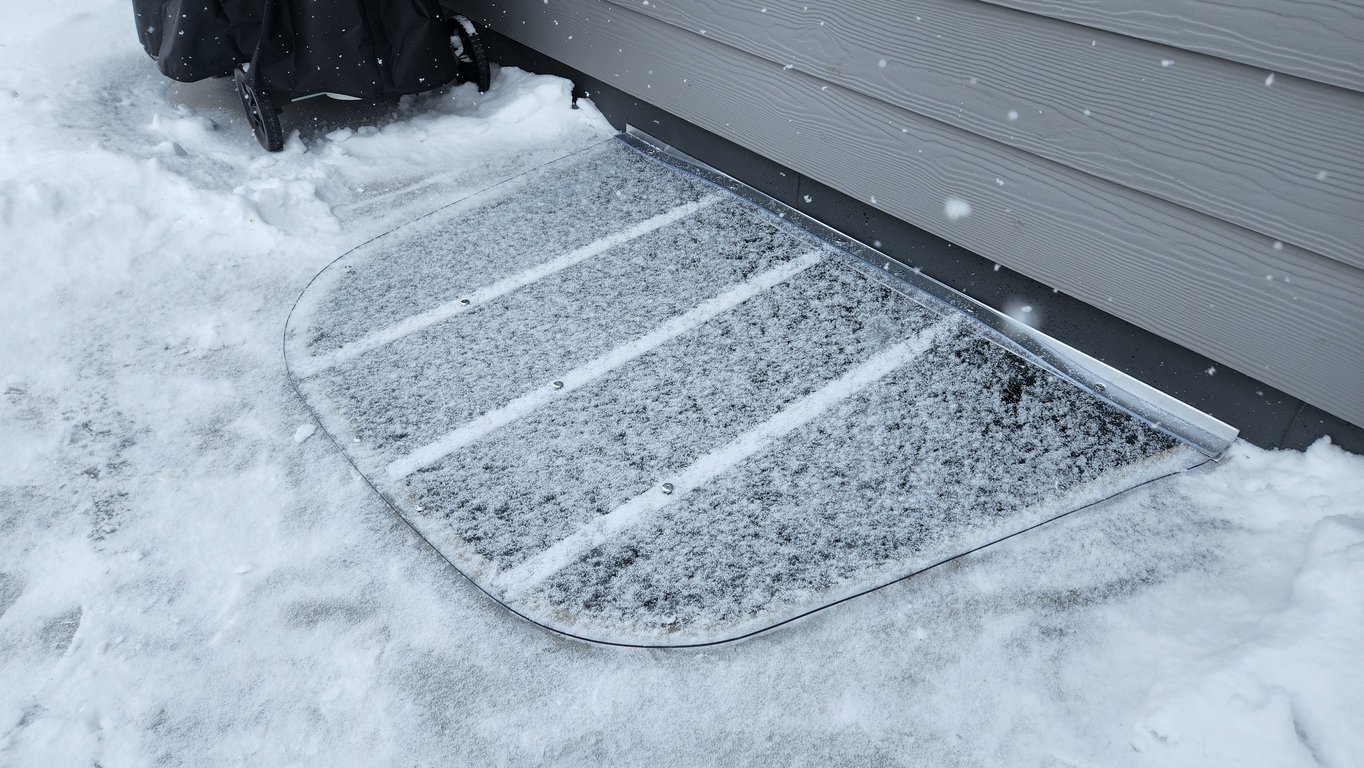 Clear polycarbonate window well cover covered in snow in Arvada Colorado showing protection from snow and rain