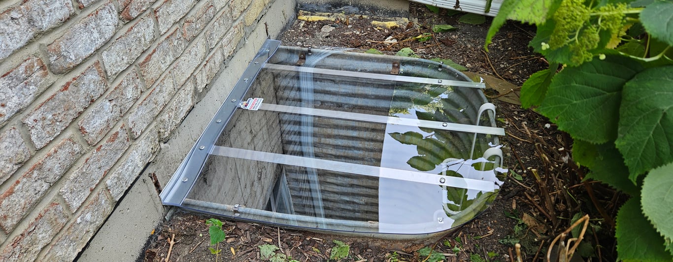 Sloped clear polycarbonate window well cover installed in Wheat Ridge Colorado to shed snow and rain