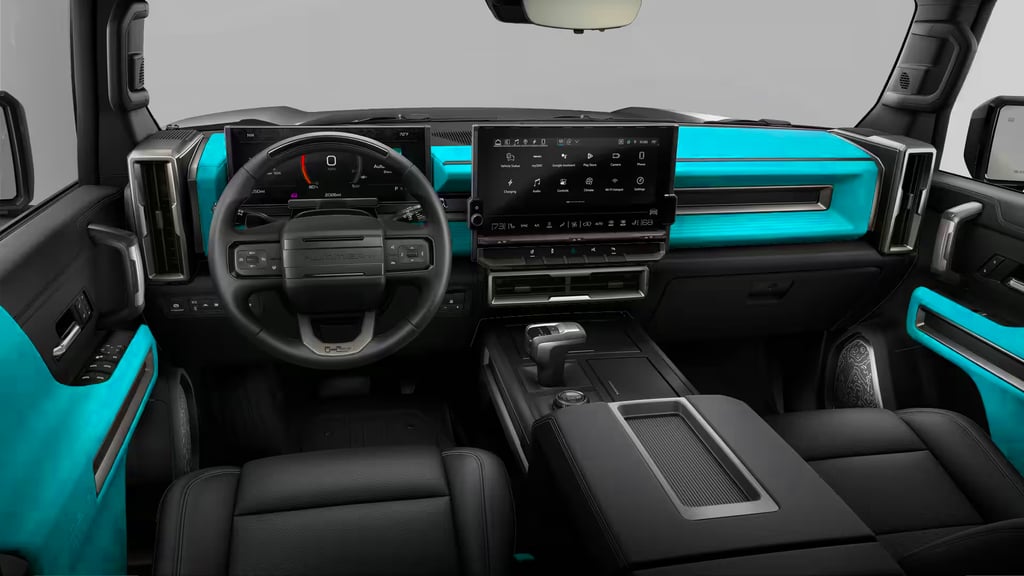 Front cabin view of the GMC HUMMER EV SUV 3X showing the wide infotainment touchscreen, digital driver display, steering wheel controls, center console shifter, and bold teal interior accents—highlighting the audio and entertainment-focused dashboard layout.