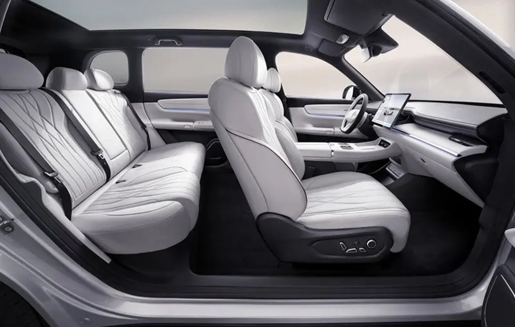 Interior view of the Changan Qiyuan Q07 showing white leather seats, spacious rear bench, panoramic glass roof, and a minimalist dashboard with a large central touchscreen.