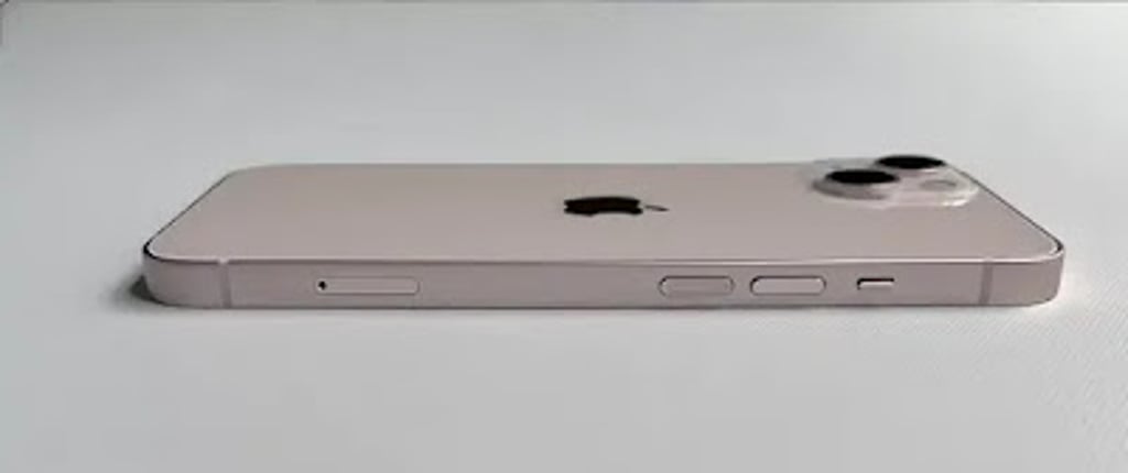 Side view of the Apple iPhone 13 lying flat on a white surface, showing the slim aluminum frame, volume buttons, mute switch, and raised dual-camera module.