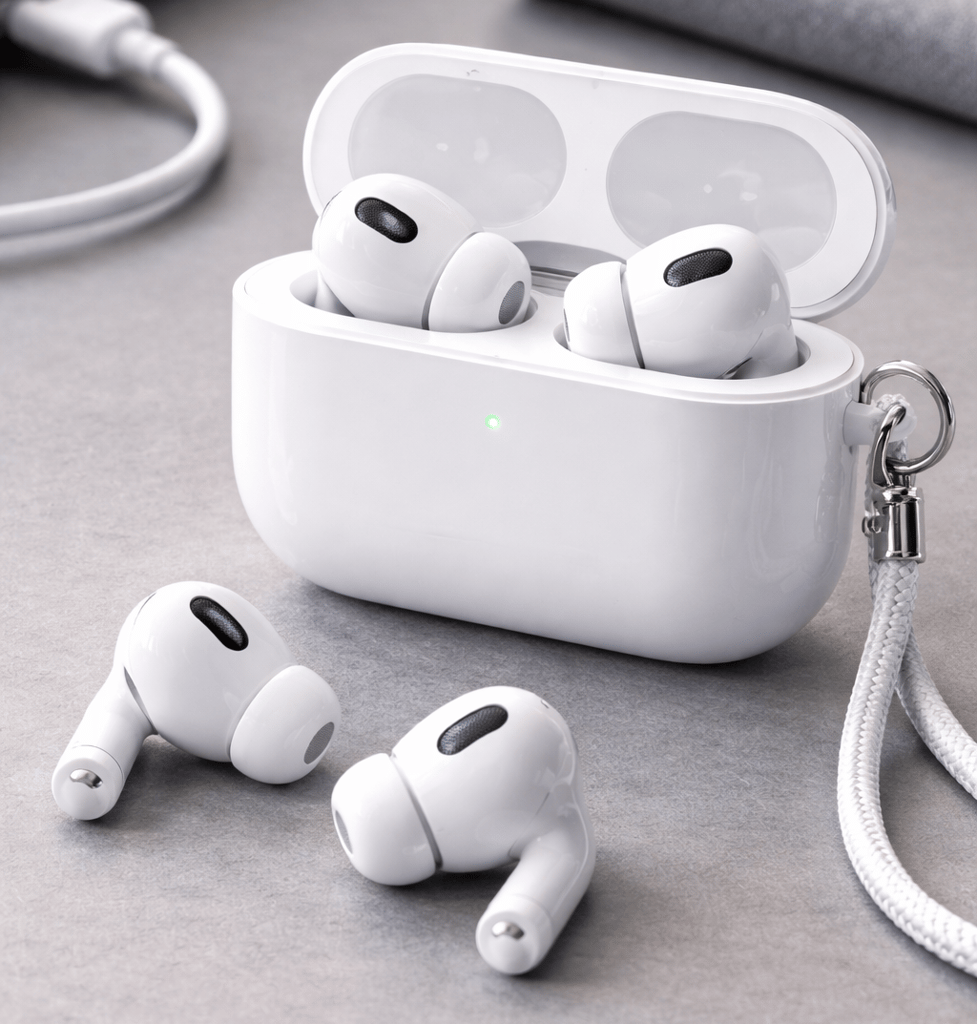 Apple AirPods Pro (2nd Generation) with charging case open on a gray desk, showing the earbuds with silicone tips and a lanyard attached to the case.