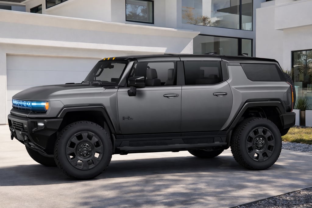 Dark gray GMC HUMMER EV SUV parked in the driveway in front of a modern white house with large glass windows and a clean minimalist exterior, showcasing its rugged stance and off-road tires.