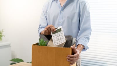 Persona empaquetando objetos personales de escritorio en una caja de cartón tras una desvinculación laboral, con una calculadora visible, representando el impacto de la automatización IA Chile en profesiones administrativas.