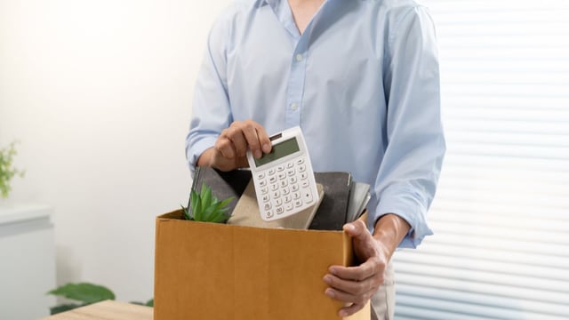 Persona empaquetando objetos personales de escritorio en una caja de cartón tras una desvinculación laboral, con una calculadora visible, representando el impacto de la automatización IA Chile en profesiones administrativas.