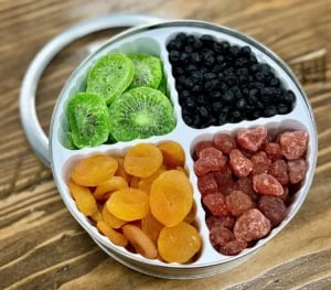 Assorted dried fruits in a round tin container divided into sections