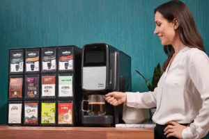 Woman brewing coffee with a Flavia C300 single-pack office coffee machine beside assorted drink options in a breakroom