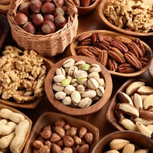 Assorted nuts displayed in wooden bowls including pistachios, pecans, walnuts, hazelnuts, and peanuts