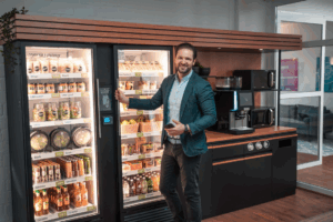 A professional standing in front of a modern micro-market vending installation filled with fresh food, drinks, and healthy options, representing the future of workplace vending in Fort Worth.