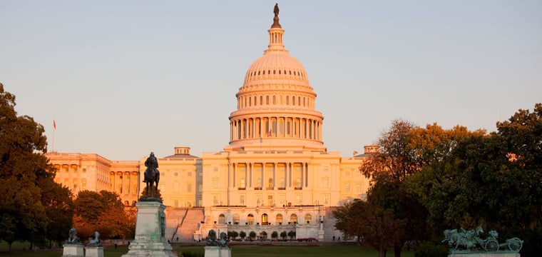 Color photograph of the United States Capitol building at sunset, its dome lit warm gold, with memorial statues and the grounds in the foreground.