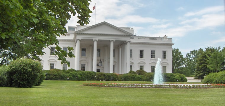 Color photograph of the North Portico of the White House, with the front lawn, fountain, and American flag flying above.