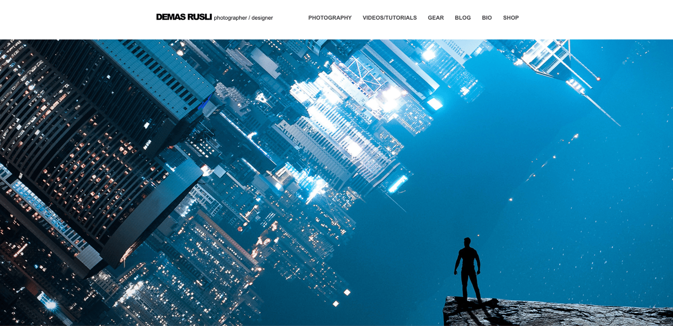 Demas Rusli's photography portfolio homepage with a dramatic full-width composite photo of a silhouetted figure at the edge of a cliff overlooking a blue-toned inverted cityscape