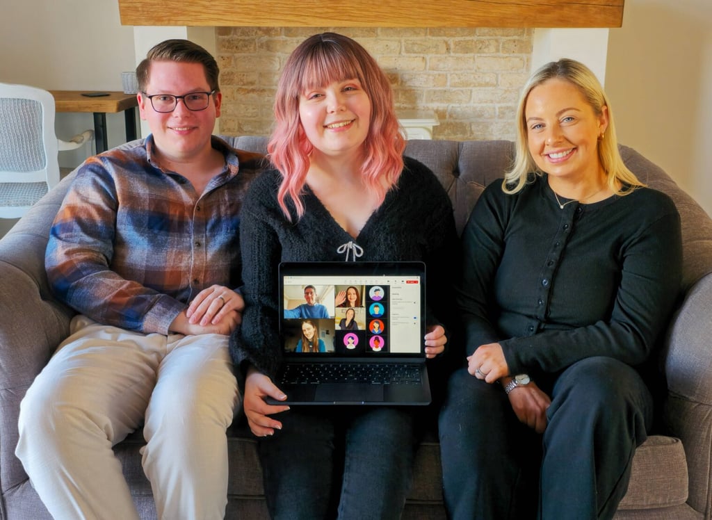 Three members of the Inkfire team sitting together on a couch, holding a laptop that shows the rest of the team joining by video call.