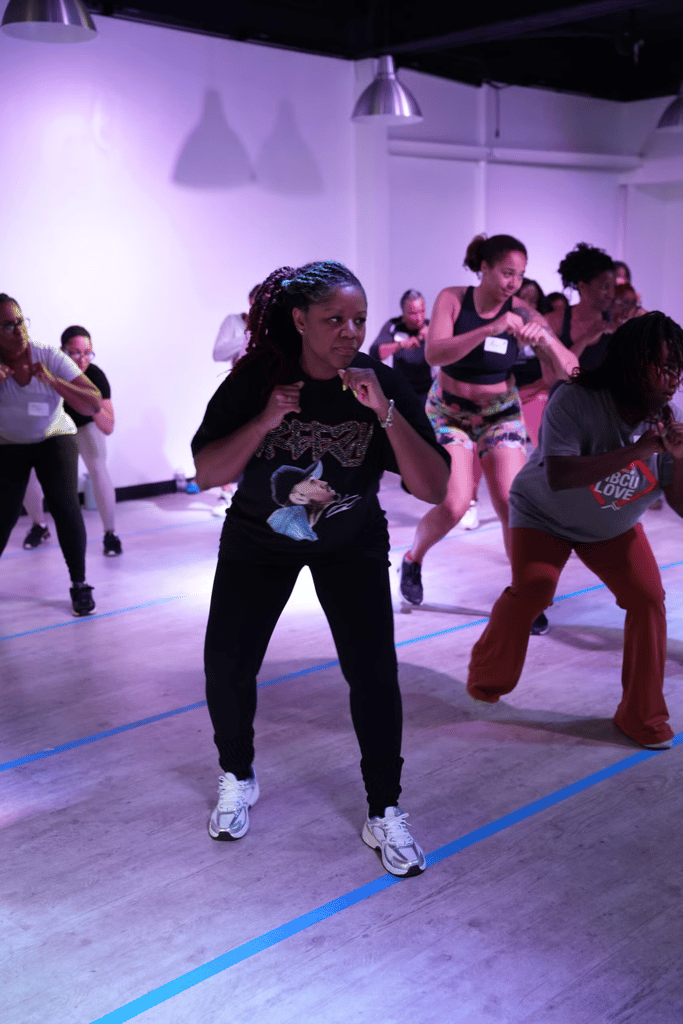 Dancers mid-routine in a Dance With Sarah Powell class, focused and in motion in a purple-lit studio.