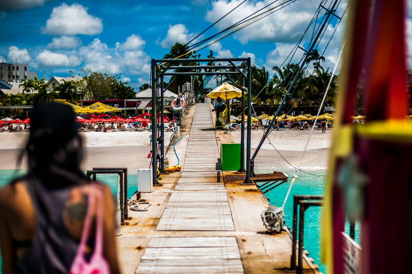 A woman walking down a dock towards a beach in Barbados