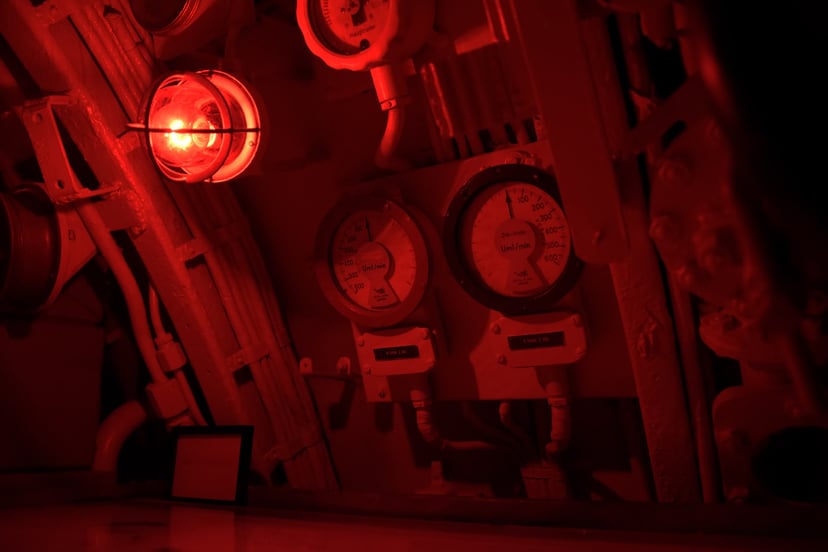 dials and gauges on a ship illuminated by a red warning light