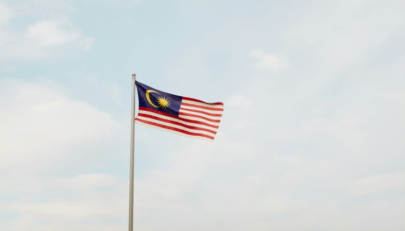 The flag of Malaysia flying against a blue sky with fluffy white clouds