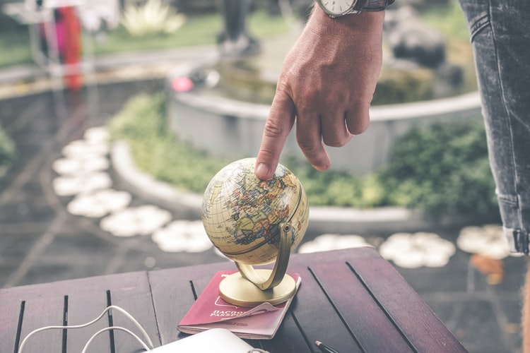a finger pointing to a spot on a mini globe